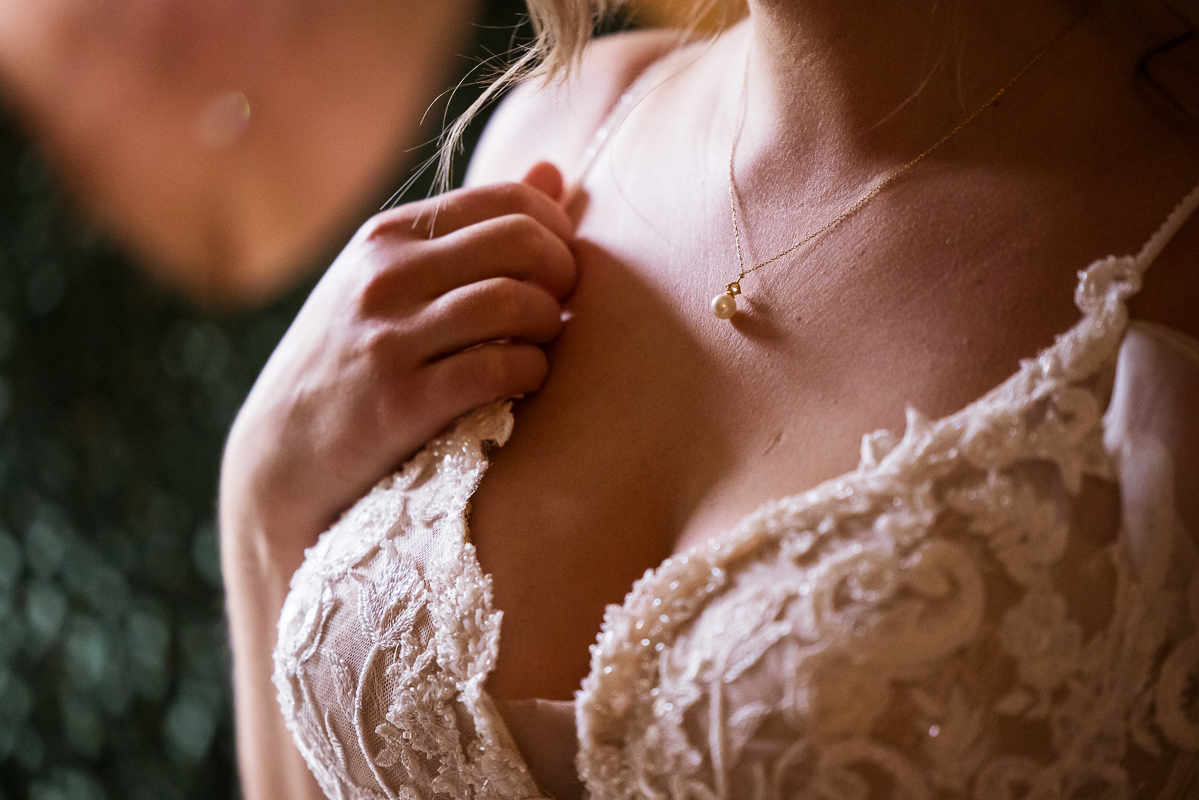 close up image of the bride as she holds the strap of her dress while showing off her peal necklace and lace detail on her wedding dress captured by best pa wedding photographer, Lisa Rhinehart