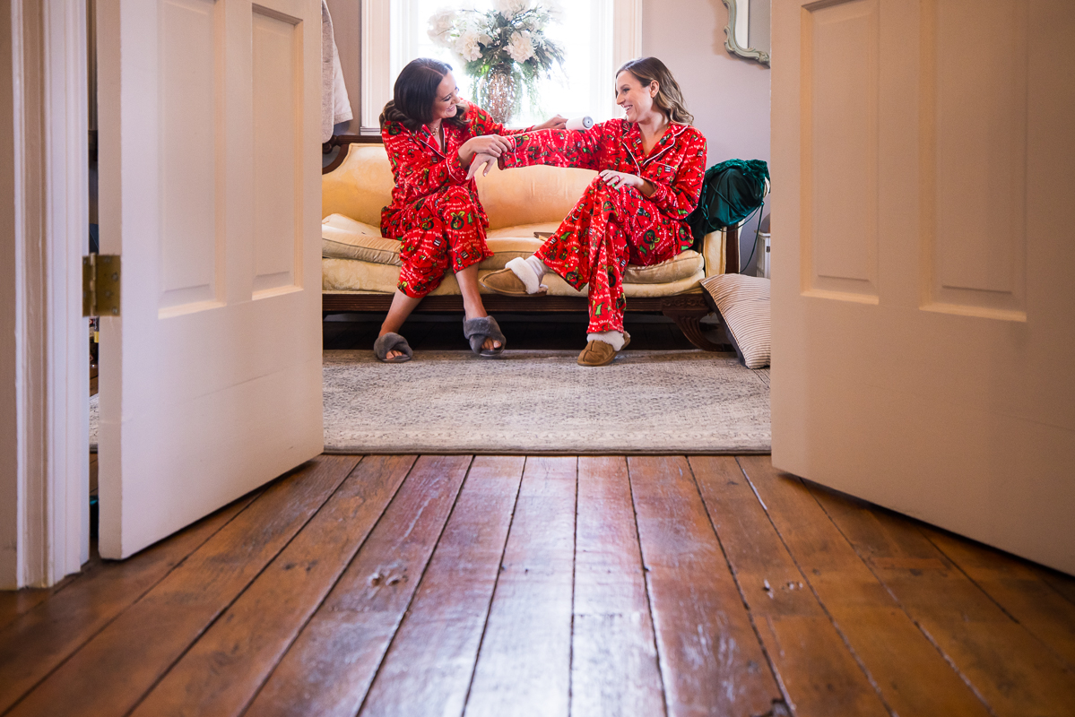 best pa wedding photographer, Lisa Rhinehart, captures this candid shot of two bridesmaids as they sit on the couch in their red grinch pjs while they wait to finish hair and makeup preparations before this outdoor Christmas wedding ceremony 
