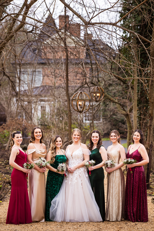 Stone Mill Inn Wedding photographer, Lisa Rhinehart, captures this bridal party as they stand together in their Christmas colored dresses underneath tree limbs and chandeliers after this outdoor Christmas wedding ceremony 