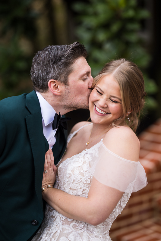 Stone Mill Inn Wedding photographer, Lisa Rhinehart, captures this fun, authentic moment between the bride and the groom as the groom kisses the bride on the cheek as she smiles during their romantic portraits before their outdoor winter wedding