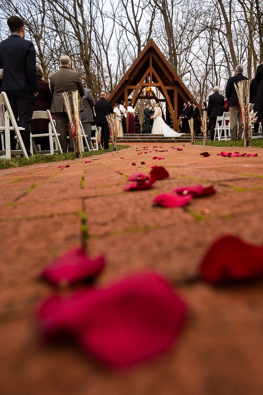 creative Stone Mill Inn Wedding photographer, Lisa Rhinehart, captures this unique perspective of the flower petals that were thrown down the aisle leading to the bride and groom holding hands at the abbey during this outdoor Christmas wedding ceremony in Hallam pa 