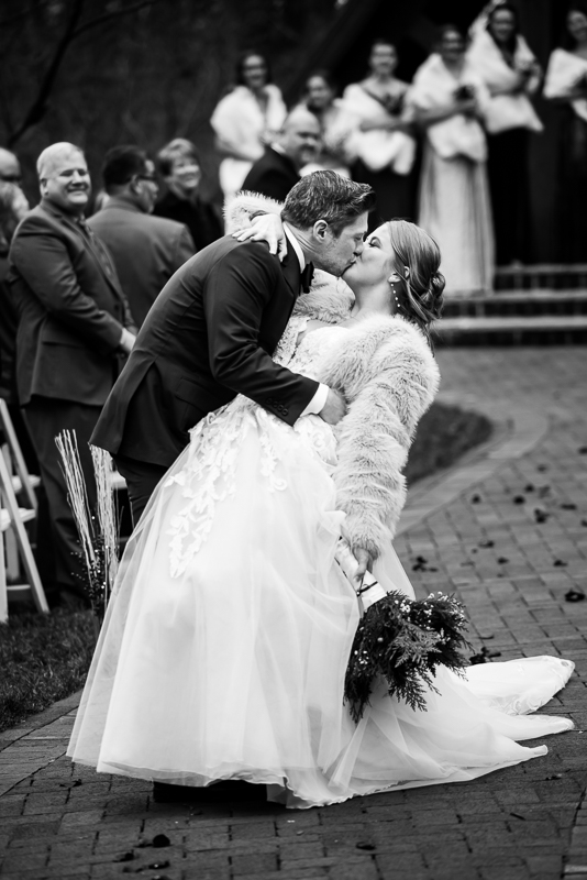 Stone Mill Inn Wedding photographer, Lisa Rhinehart, captures this black and white image of the bride and groom as they share a kiss while walking down the aisle at this outdoor Christmas wedding ceremony in Hallam pa 