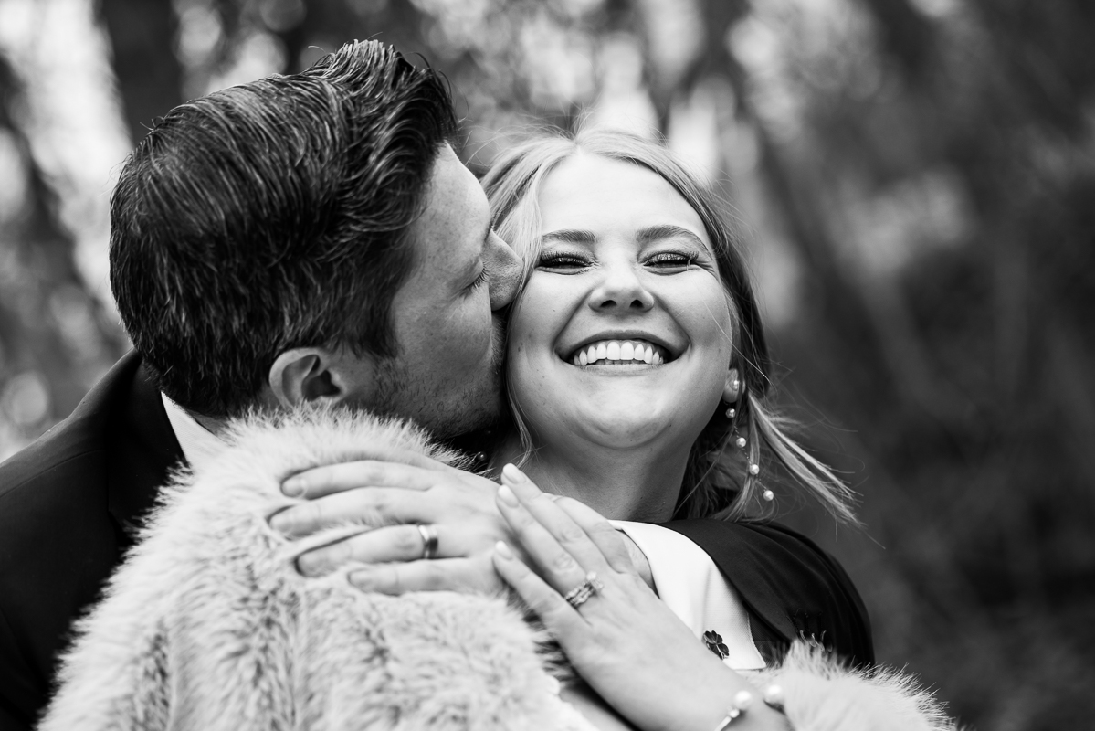 Stone Mill Inn Wedding photographer, Lisa Rhinehart, captures this authentic moment between the bride and groom as the groom kisses the brides cheek while she smiles during their romantic golden hour portrait session after their outdoor Christmas wedding ceremony 