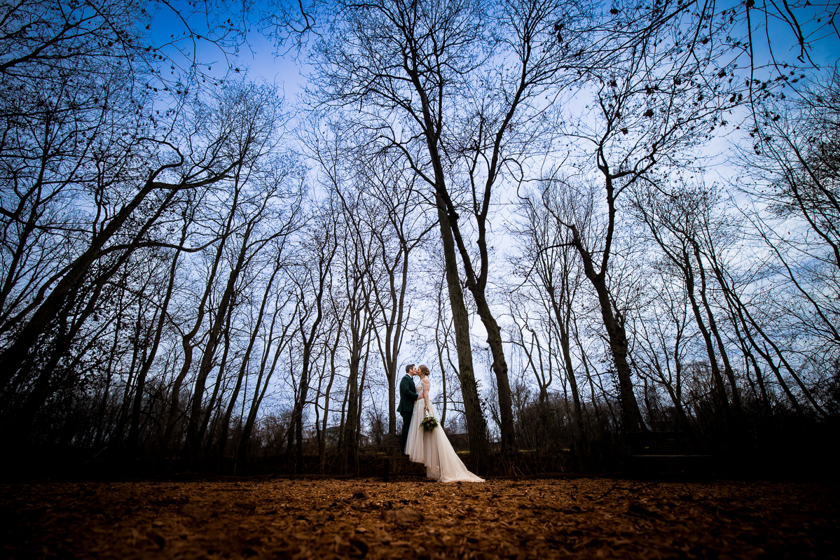 Stone Mill Inn Wedding photographer, Lisa Rhinehart, captures this unique image of the bride and groom as they kiss in front surrounded by trees during their romantic portraits after their Christmas wedding ceremony 