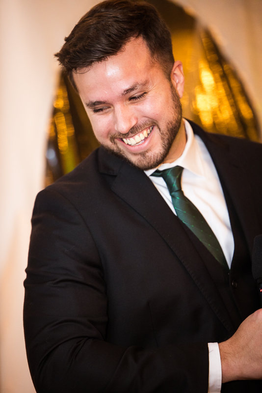 candid wedding photographer, Lisa Rhinehart, captures this image of a groomsmen as he smiles and laughs while giving his speech during the traditions portion of this winter wedding reception 