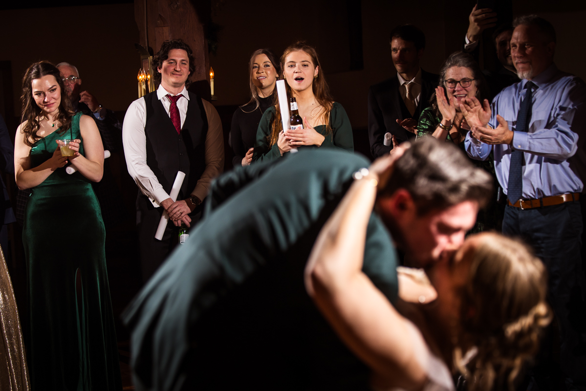 candid image of family and friends watching the bride and groom as they share a kiss during their choreographed first dance at this winter wedding reception 