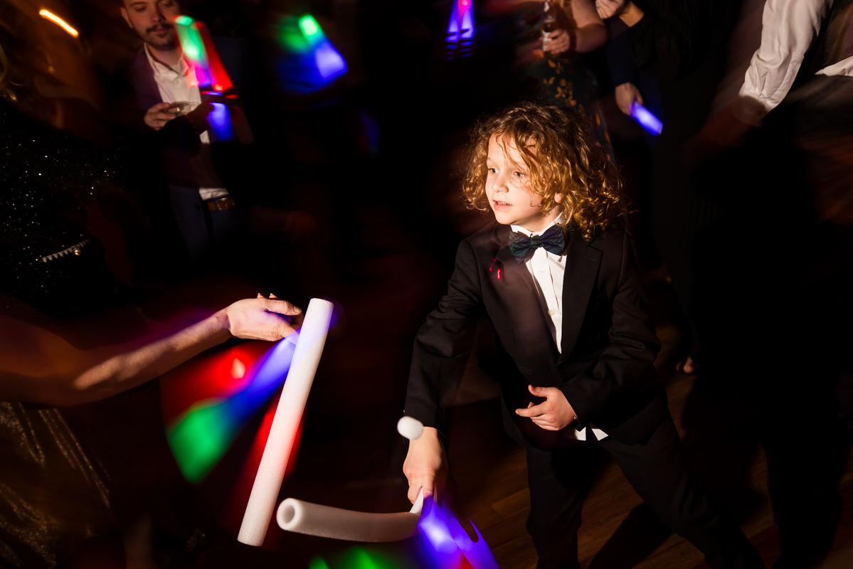 image of a young boy as he is surrounded by the colorful glow sticks while dancing during this winter wedding reception 