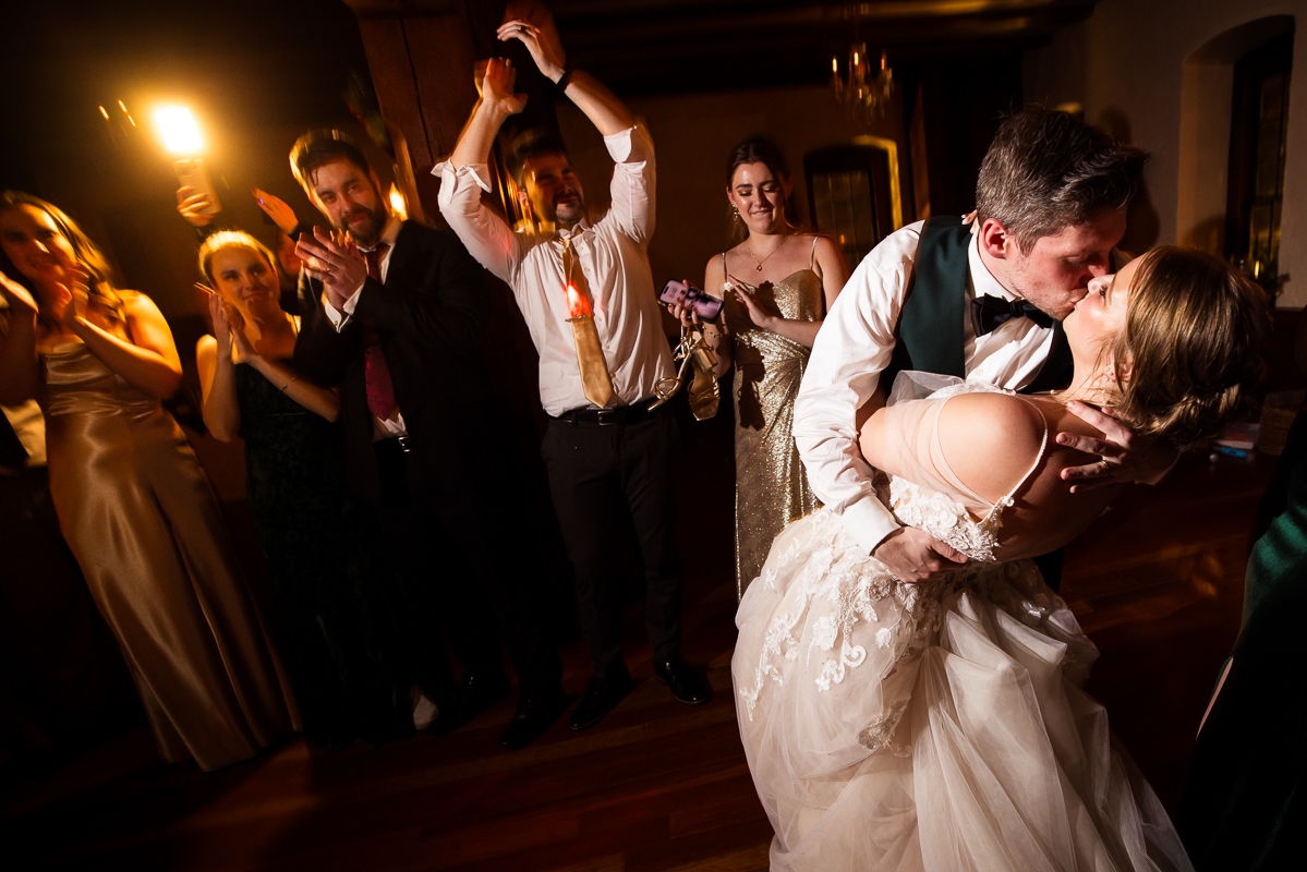 Stone Mill Inn Wedding photographer, Lisa Rhinehart, captures this image of the bride and groom as they share a kiss on the dance floor together while their family and friends cheer and clap for them 