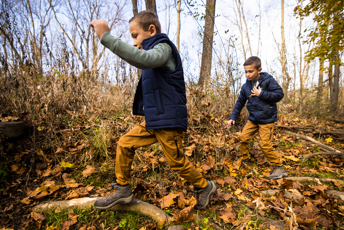 photojournalist photographer, Lisa Rhinehart, captures this fun, candid moment of the two brothers running through the woods chasing each other during this fall outdoor family session at wildlands conservancy in Emmaus pa 