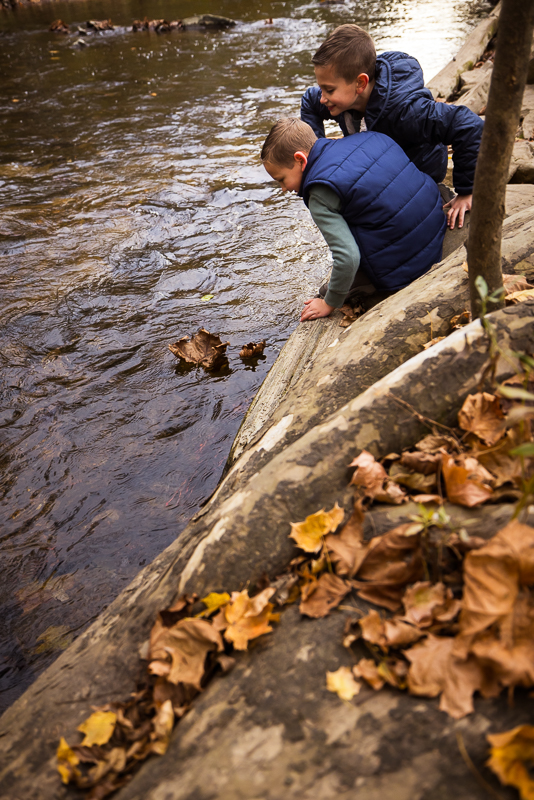 pa family photographer, Lisa Rhinehart, captures this fun, candid playful image of the two boys as they race leaves down the stream together inside of the wildlands conservancy in emmaus pa with Lehigh valley family photographer