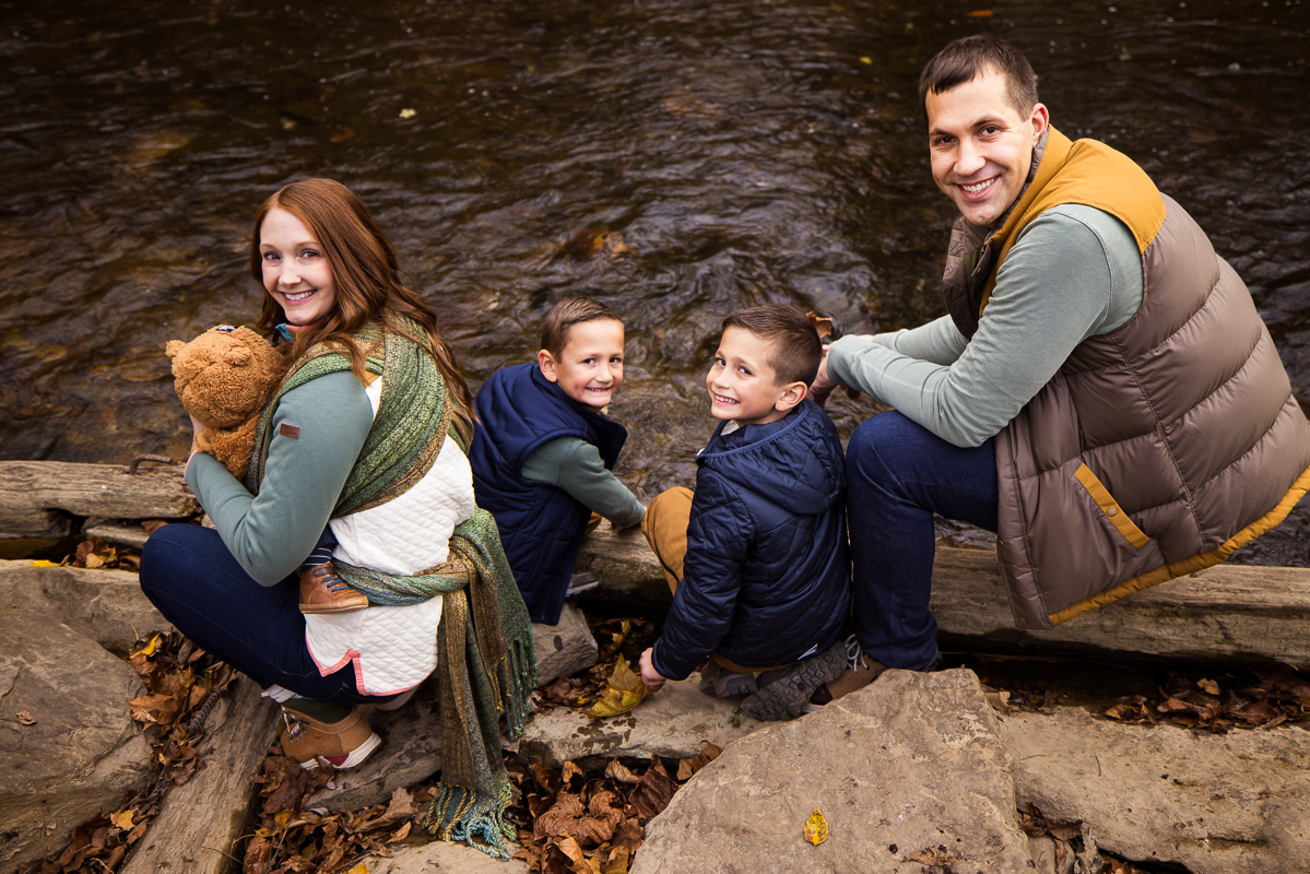 outdoor family photographer, Lisa Rhinehart, captures this nice traditional family portrait of the family outside together as they sit by the water and race leaves together at the wildlands conservancy in Lehigh Valley 