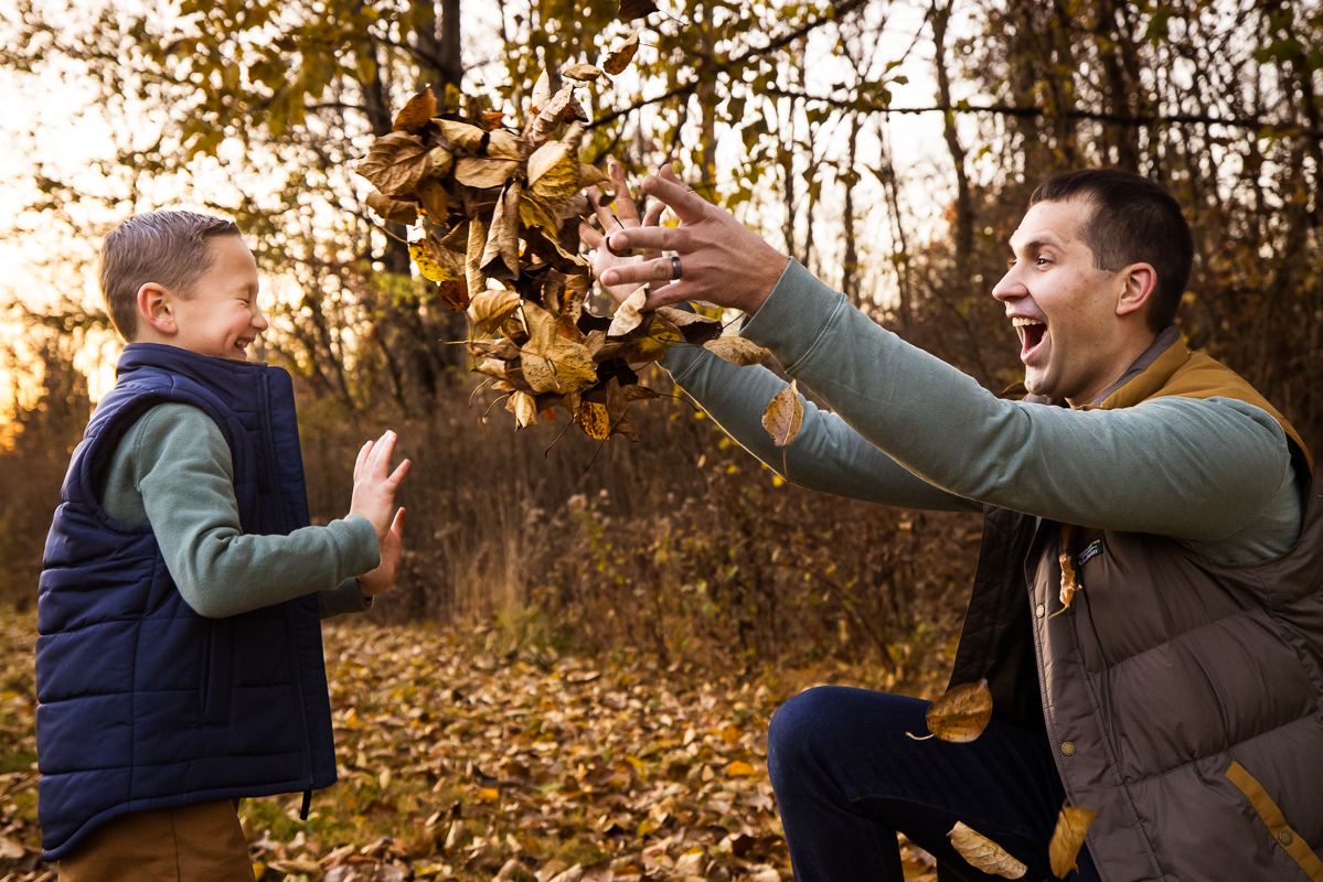 Lehigh Valley family photographer, Lisa Rhinehart, captures this fun, candid playful moment of the dad and his son as they play together in the fall leaves and throw them around during this outdoor fall family session in Lehigh Valley 