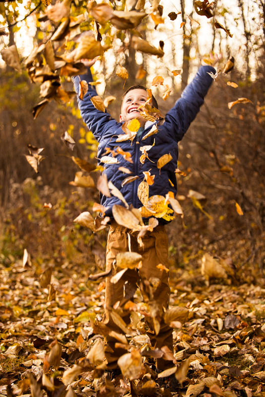 Lehigh Valley family photographer, Rhinehart Photography, captures this fun, candid, authentic moment of the son playing with colorful fall leaves and throwing them in the air during this wildlands conservancy photojournalism session in emmaus, pa 