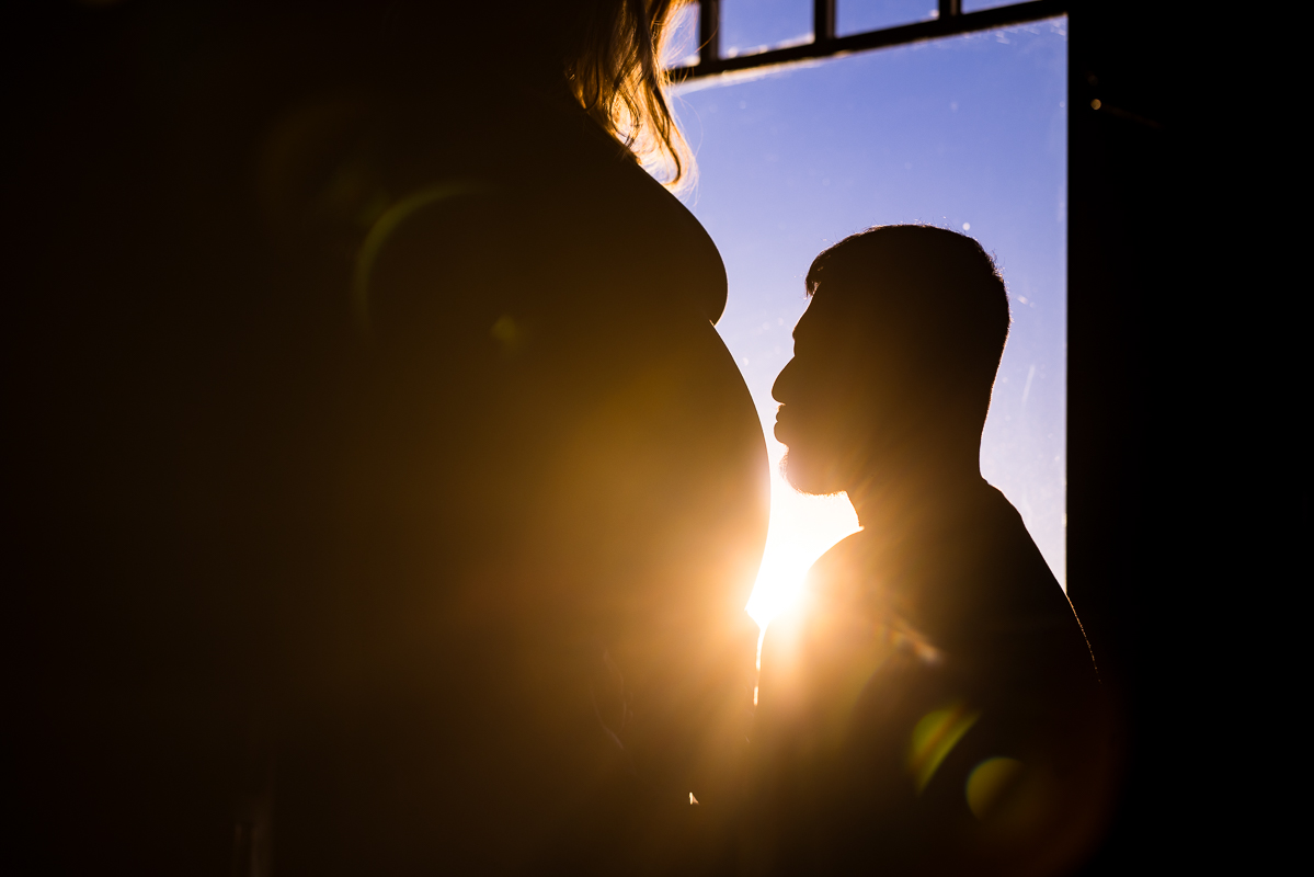 Creative Mechanicsburg family photographer, Lisa Rhinehart, captures this unique portrait of the husband and wife as they stand together in front of the window while the sun beams in on them creating a silhouette during this willows at ashcombe mansion maternity session in central pa 