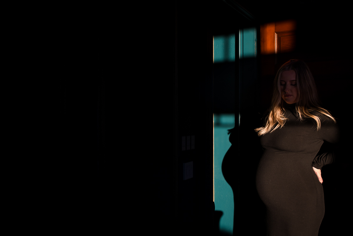 dark, moody image of the wife as she shows off her baby bump in the beam of sunlight during this creative, unique maternity session in central pa 