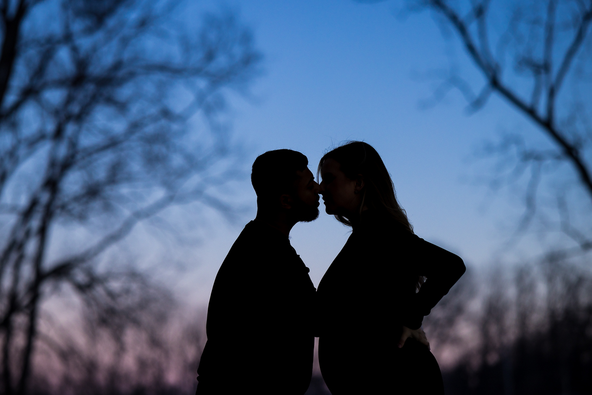 Creative Mechanicsburg family photographer, Lisa Rhinehart, captures this nighttime silhouette portrait of the couple with a blue and pink sky behind him during their maternity session at the willows at ashcombe mansion in mechanicsburg pa 