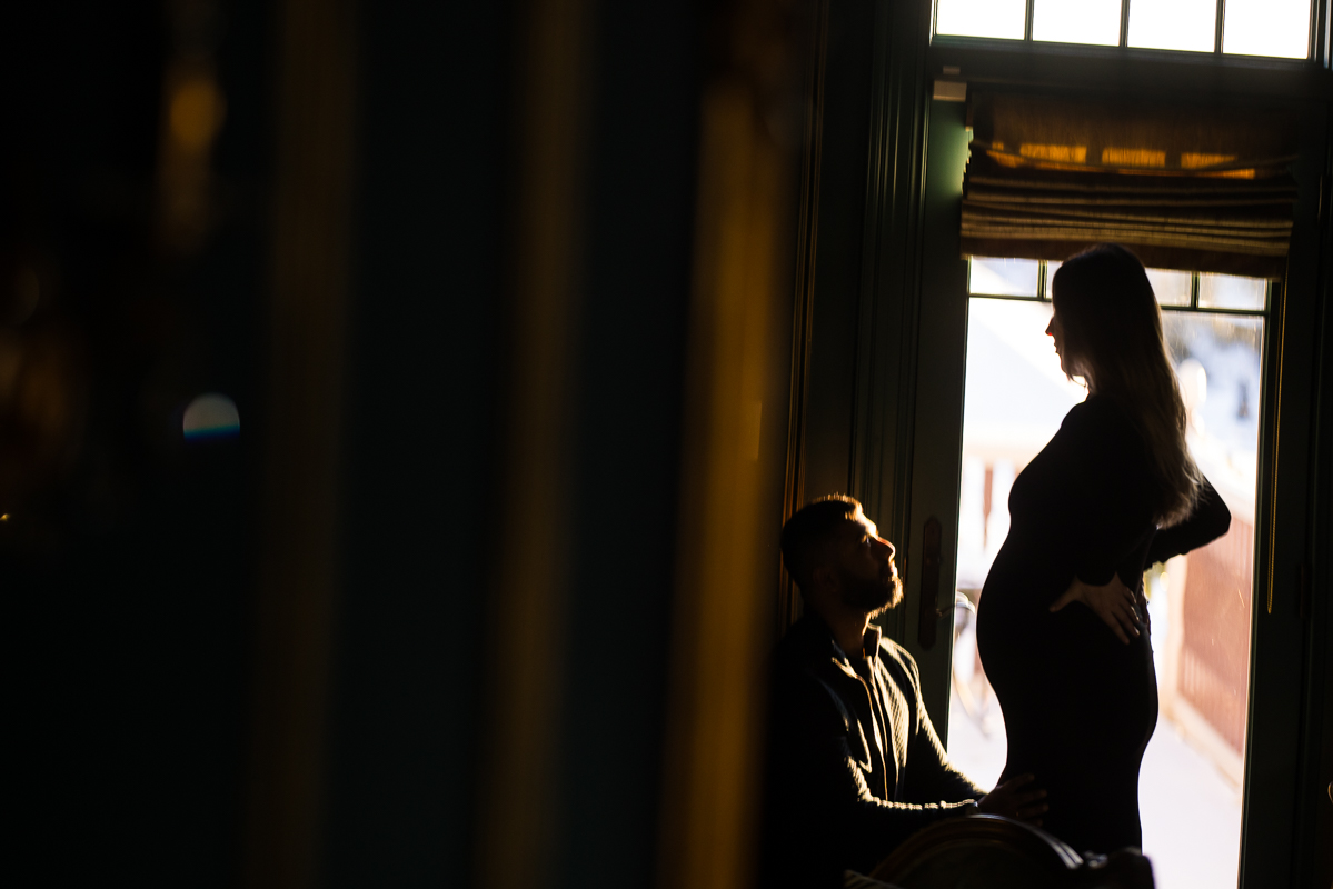 Creative Mechanicsburg family photographer, Lisa Rhinehart, captures this creative, unique image of the couple as they stand together in front of the window during this cozy, moody maternity session inside of the ashcombe mansion in central pa 
