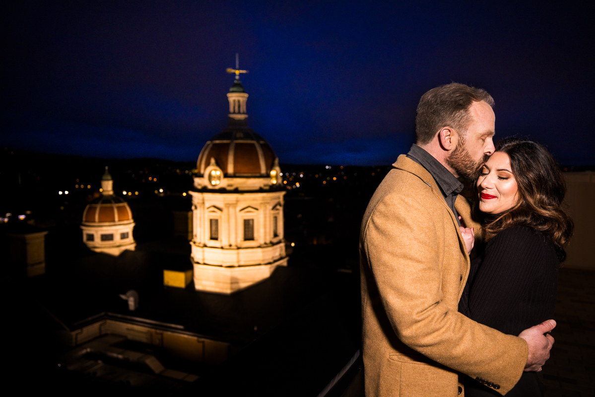 candid engagement photographer, Lisa Rhinehart, captures this image of the couple as they share a kiss on the forehead on the rooftop of the Yorktowne hotel in pa 