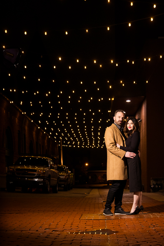 traditional portrait of the couple as they embrace one another during these night time portraits on the red brick walkway with twinkle lights above them during this York pa engagement session 
